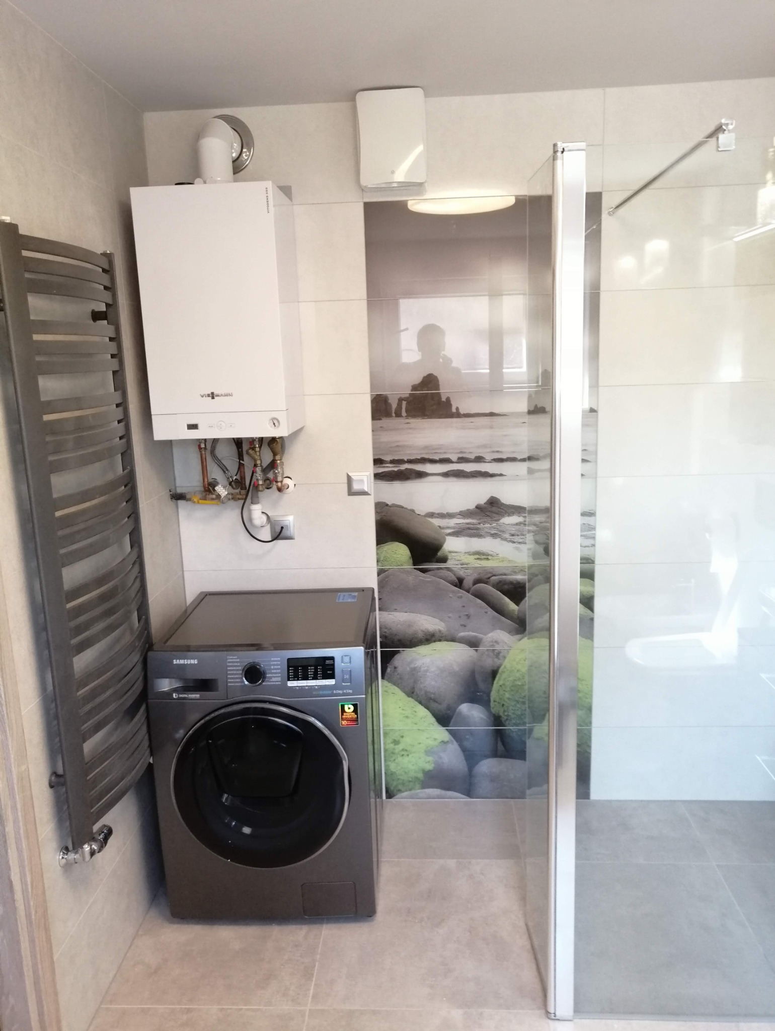 Nowoczesna łazienka z pralką Samsung, grzejnikiem drabinkowym i bojlerem Viessmann. Na ścianie dekoracyjne płytki z motywem nadmorskim. Kabina prysznicowa ze szklanymi drzwiami.