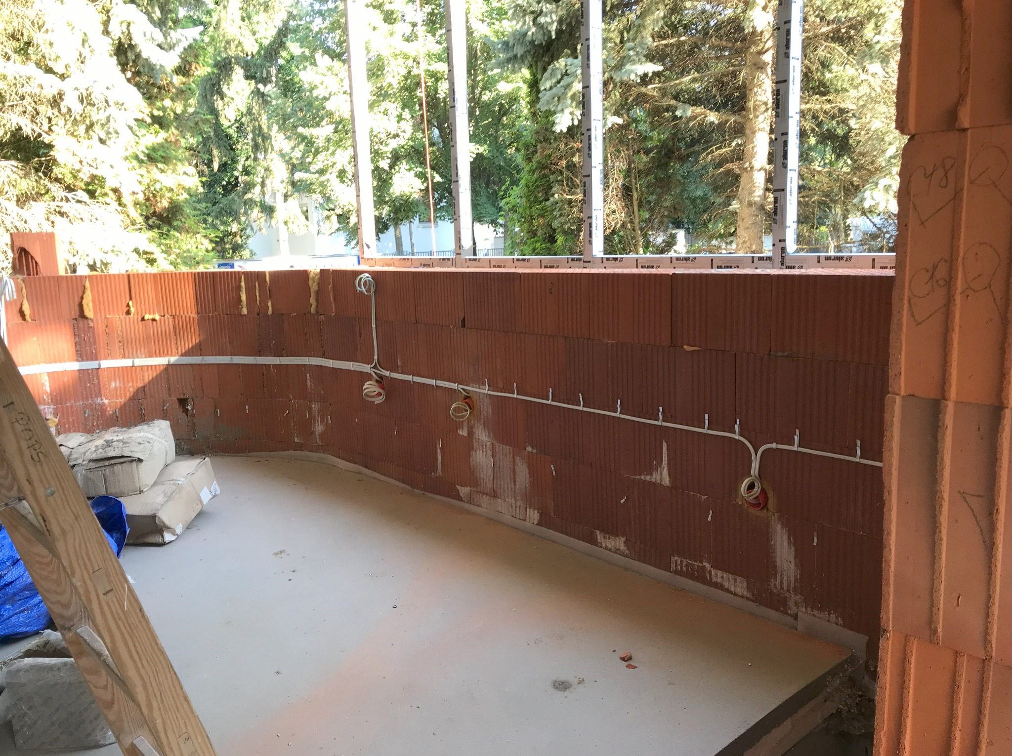 Wewnętrzne okablowanie elektryczne w nowo budowanym domu z czerwonej cegły, widoczne puszki instalacyjne i przewody, na podłodze leżą kartony i drabina.