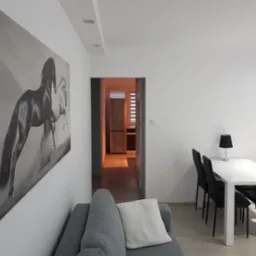 Jasne wnętrze mieszkania z szarą sofą, białym stołem z czarnymi krzesłami i obrazem z motywem koni na ścianie.