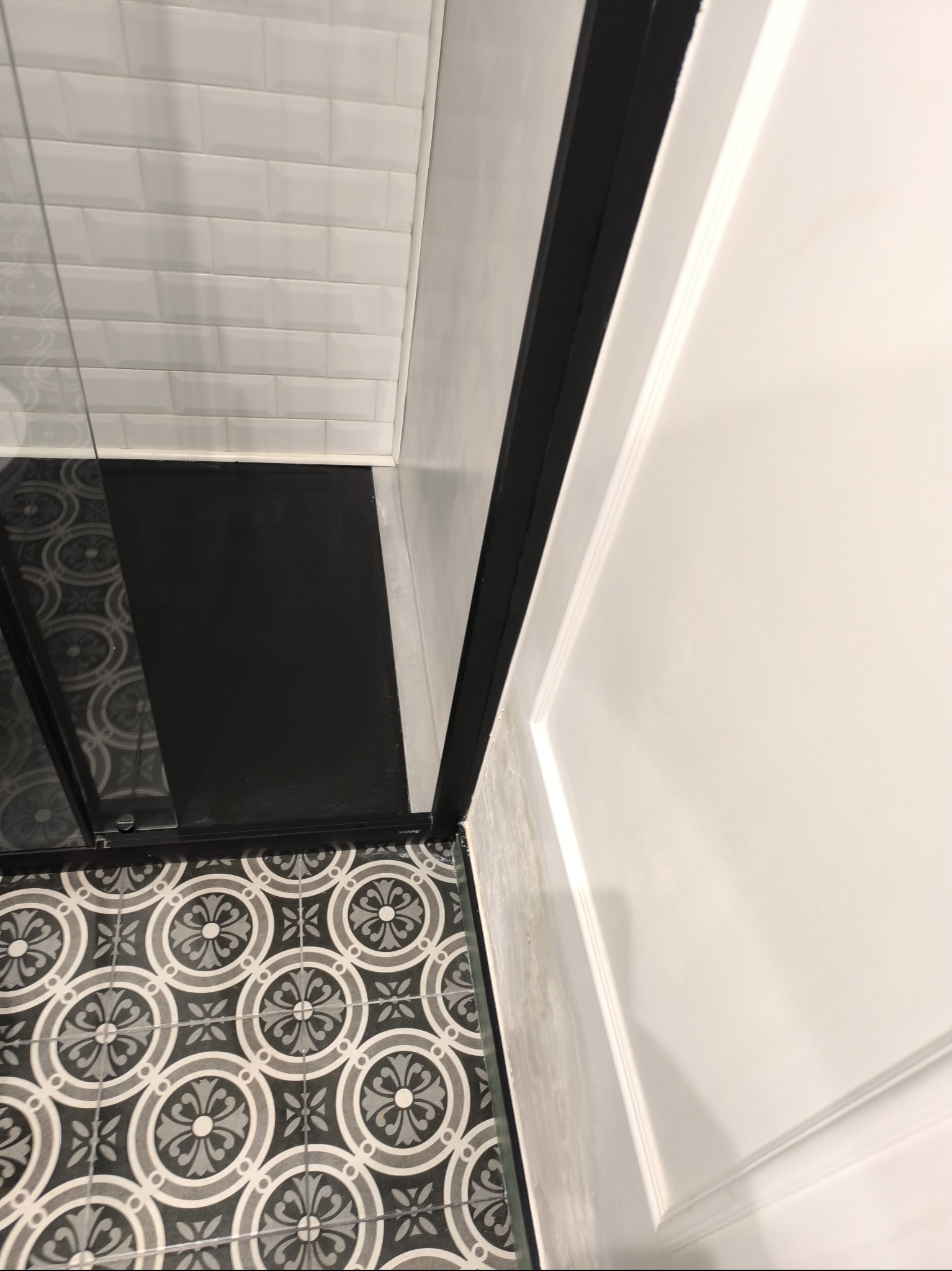 Czarno-biała łazienka z wzorzystą podłogą, białe płytki ścienne typu metro i czarna rama kabiny prysznicowej, widok z góry.