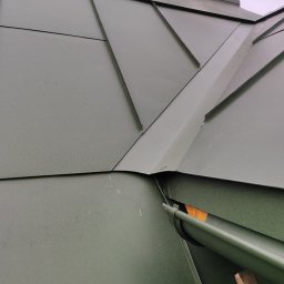 Marcin Michalkiewicz - Szczegółowe ujęcie fragmentu dachu z blachy w odcieniach zieleni, z widocznymi obróbkami blacharskimi i fragmentem rynny, uchwycone pod kątem.
