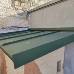 Nowy, zielony daszek nad wejściem, zamontowany na nierównych ścianach z kamienia i tynku, widoczny z bliska.