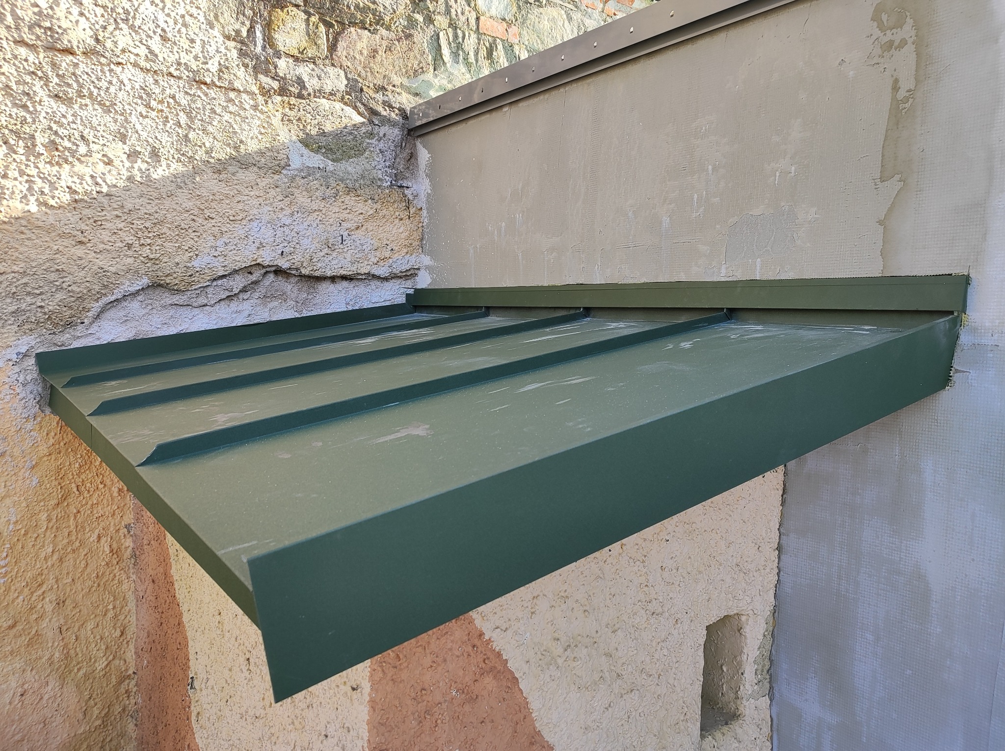 Nowy, zielony daszek nad wejściem, zamontowany na nierównych ścianach z kamienia i tynku, widoczny z bliska.