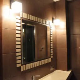 Nowoczesna łazienka z brązowymi płytkami, lustrem z dekoracyjną ramą i oświetleniem punktowym.