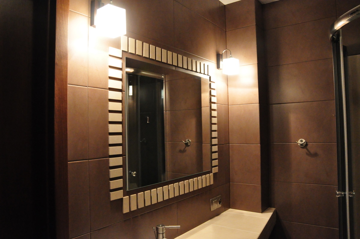 Nowoczesna łazienka z brązowymi płytkami, lustrem z dekoracyjną ramą i oświetleniem punktowym.