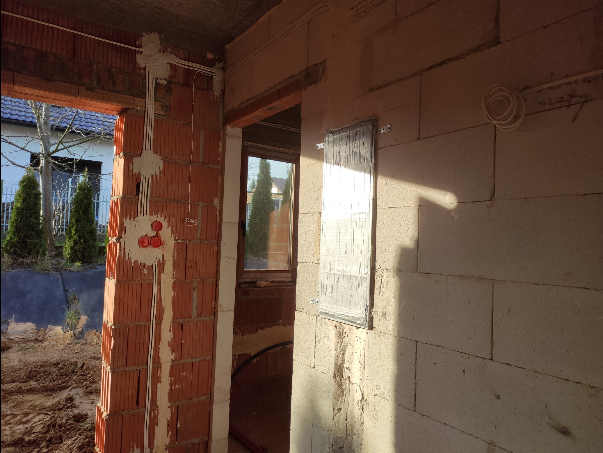 Wnętrze w trakcie budowy: widoczne przewody elektryczne w ścianie z cegły, puszki instalacyjne i fragment instalacji na ścianie z betonu komórkowego.
