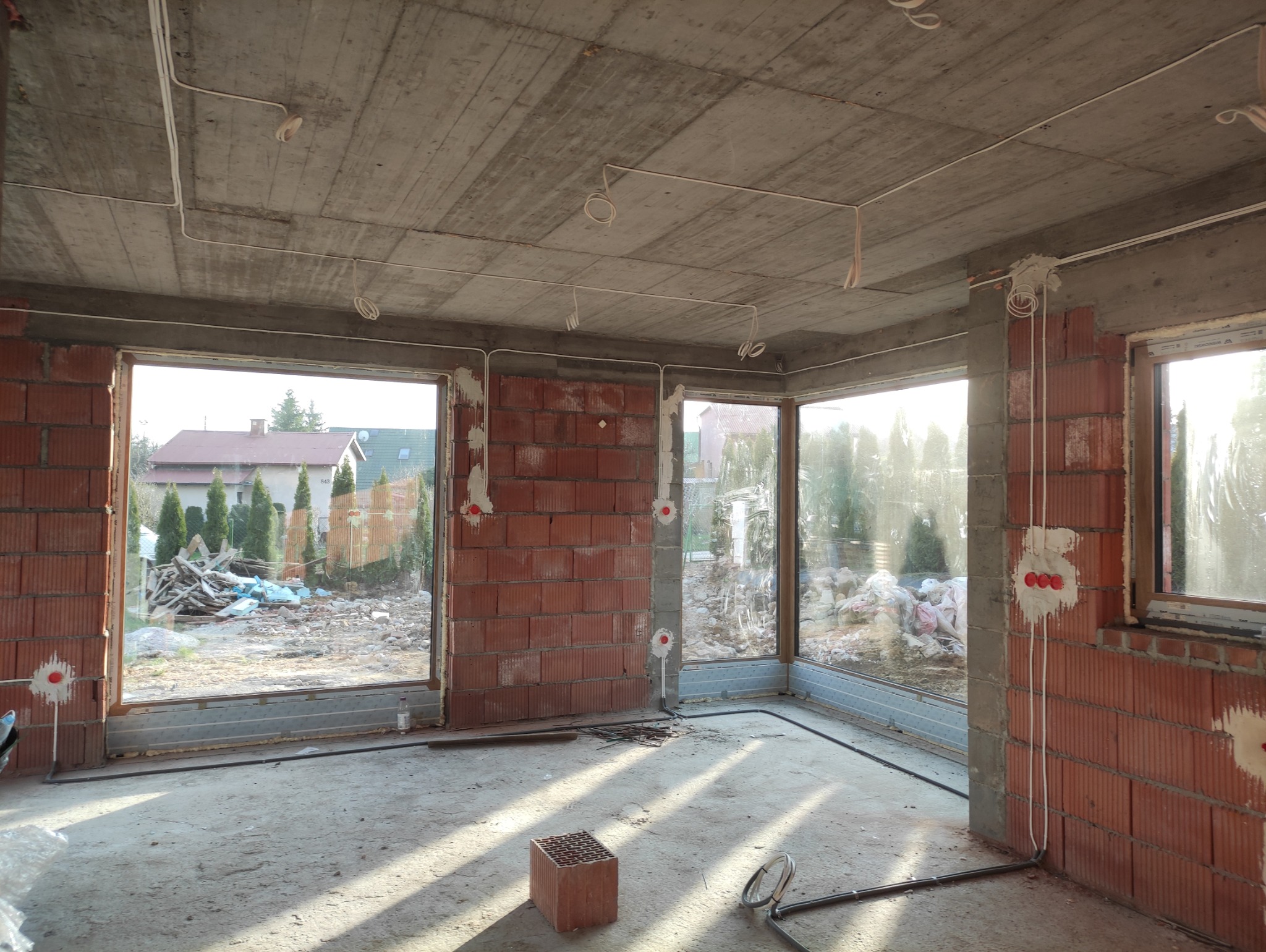 Surowy stan: Instalacja elektryczna w nowym domu z cegły. Widoczne kable na suficie i ścianach, puszki elektryczne. Okna bez parapetów. Cegła dziurawka.