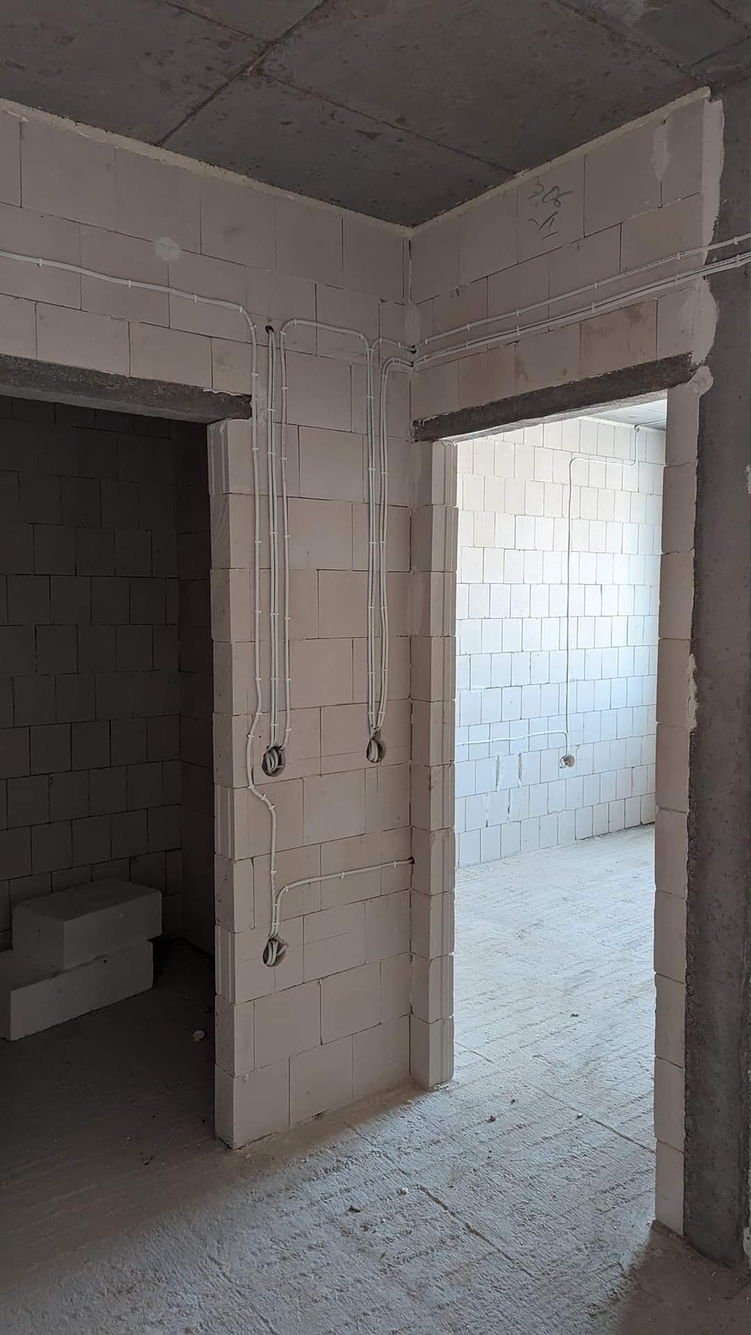 Surowe wnętrze z widoczną instalacją elektryczną w białych rurkach na ścianach z betonu komórkowego. Widoczne otwory drzwiowe i surowa podłoga.