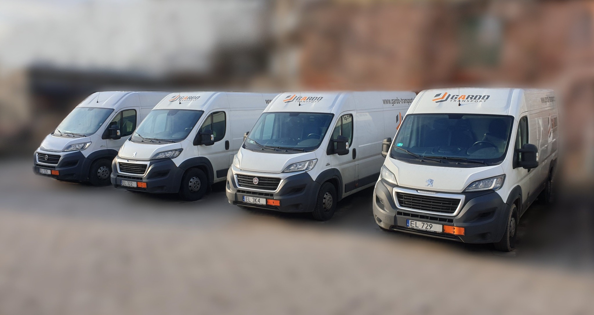 Flota czterech białych busów transportowych marki Fiat i Peugeot z logo firmy Gardo Transport, zaparkowanych w rzędzie na zewnątrz budynku.