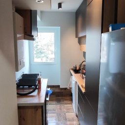 DOM-MAJSTER Michał Siemieniuk - Wąska kuchnia z drewnianą podłogą imitującą panele, ciemnymi szafkami i oświetleniem punktowym na suficie.