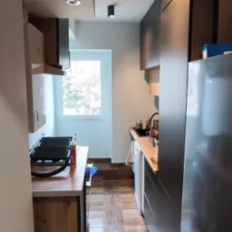 Wąska kuchnia z drewnianą podłogą imitującą panele, ciemnymi szafkami i oświetleniem punktowym na suficie.