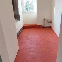 DOM-MAJSTER Michał Siemieniuk - Pokój w trakcie prac przygotowawczych do malowania podłogi na czerwono, zabezpieczone ściany i podłoga folią malarską, widoczne grzejniki i instalacja elektryczna.