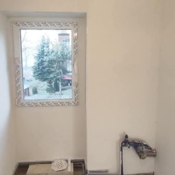 DOM-MAJSTER Michał Siemieniuk - Świeżo pomalowane ściany na biało w pomieszczeniu z oknem PCV, widoczne przygotowane przyłącze wodne i instalacja elektryczna bez osprzętu.