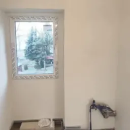 Świeżo pomalowane ściany na biało w pomieszczeniu z oknem PCV, widoczne przygotowane przyłącze wodne i instalacja elektryczna bez osprzętu.