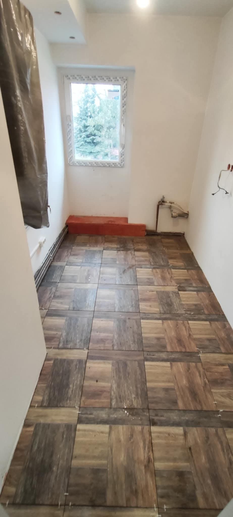 Ułożona podłoga z płytek imitujących drewno w pomieszczeniu w Lubaniu, widoczne niedociągnięcia w spoinach i przygotowane do położenia płytki przy ścianie.