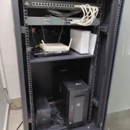 Szafa rack z zamontowanym sprzętem sieciowym: switch TP-Link, router, serwer NAS Synology, zasilacz awaryjny APC, patch panel Linkbasic i okablowanie Cat6.