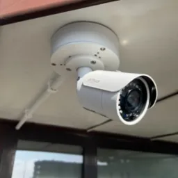 Biała kamera monitoringu Dahua zamontowana pod sufitem, widoczne okablowanie i oświetlenie LED w obiektywie.