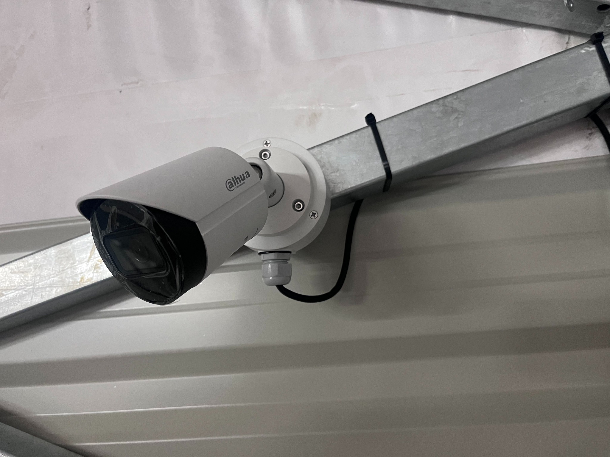 Kamera przemysłowa Dahua zamontowana na metalowej konstrukcji, widoczna na tle białej, blaszanej ściany.
