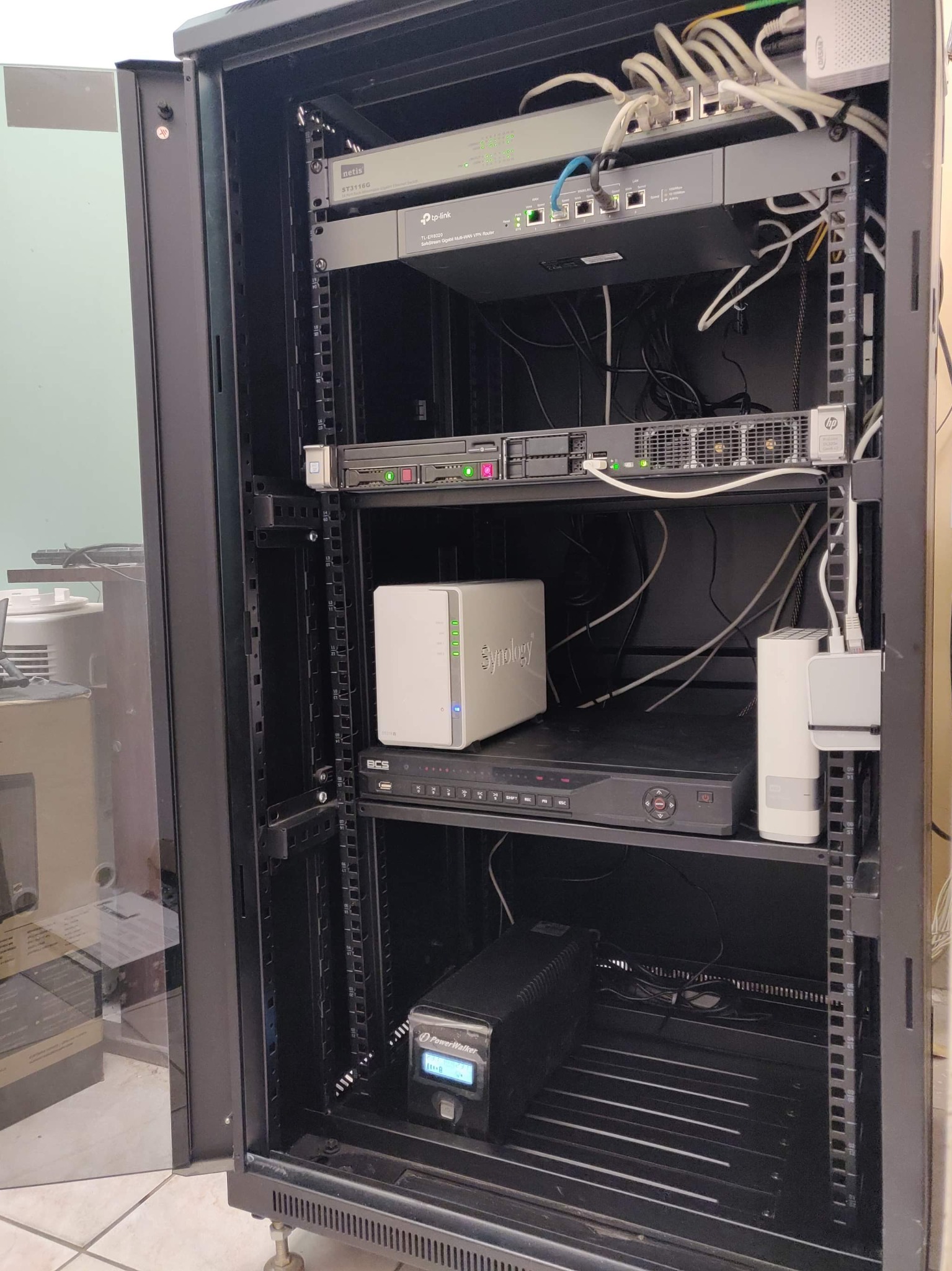 Szafa rack z zainstalowanymi urządzeniami sieciowymi: router TP-Link, serwer HP, NAS Synology, rejestrator BCS, switch Netis, zasilacz awaryjny PowerWalker oraz okablowanie.