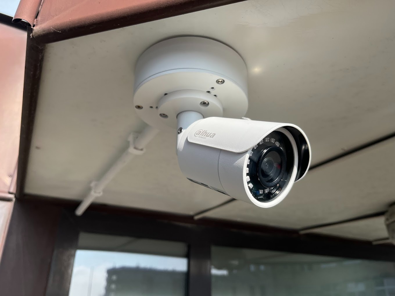 Biała kamera monitoringu Dahua zamontowana pod sufitem, widoczne okablowanie i oświetlenie LED w obiektywie.