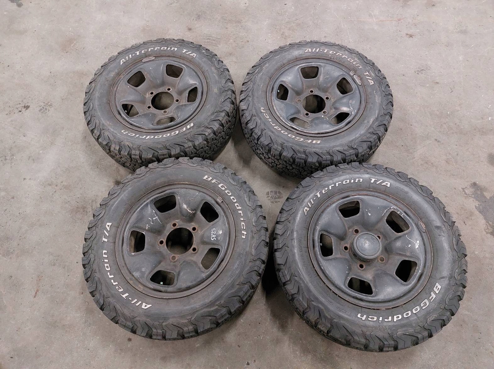 Cztery czarne felgi z oponami BFGoodrich All-Terrain T/A leżące na szarej betonowej posadzce, widoczne ślady użytkowania.