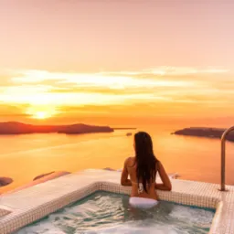 Kobieta w bikini relaksuje się w jacuzzi z widokiem na pomarańczowy zachód słońca nad morzem, Santorini.