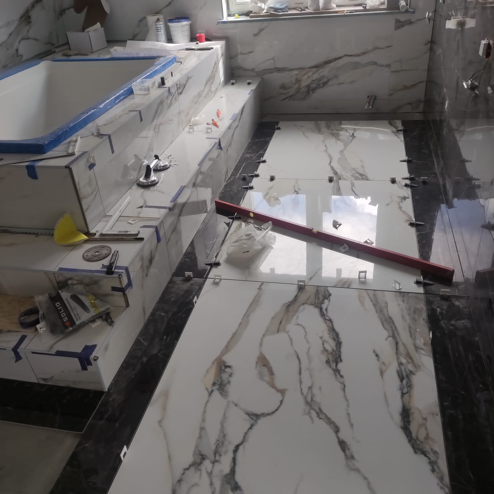 Łazienka w trakcie układania płytek imitujących marmur, widoczny poziomica, przyssawki do płytek i krzyżyki dystansowe.