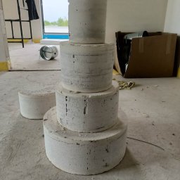 INNS SPÓŁKA Z OGRANICZONĄ ODPOWIEDZIALNOŚCIĄ - Cztery betonowe kręgi ułożone jeden na drugim w pomieszczeniu w trakcie remontu, widoczny metalowy kanał wentylacyjny i karton, w tle drabina i okno.