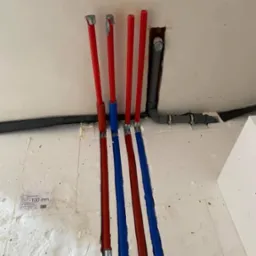 Instalacja rur PEX czerwonych i niebieskich w bruzdach w ścianie i podłodze, z widocznymi złączkami i fragmentem instalacji kanalizacyjnej w tle.