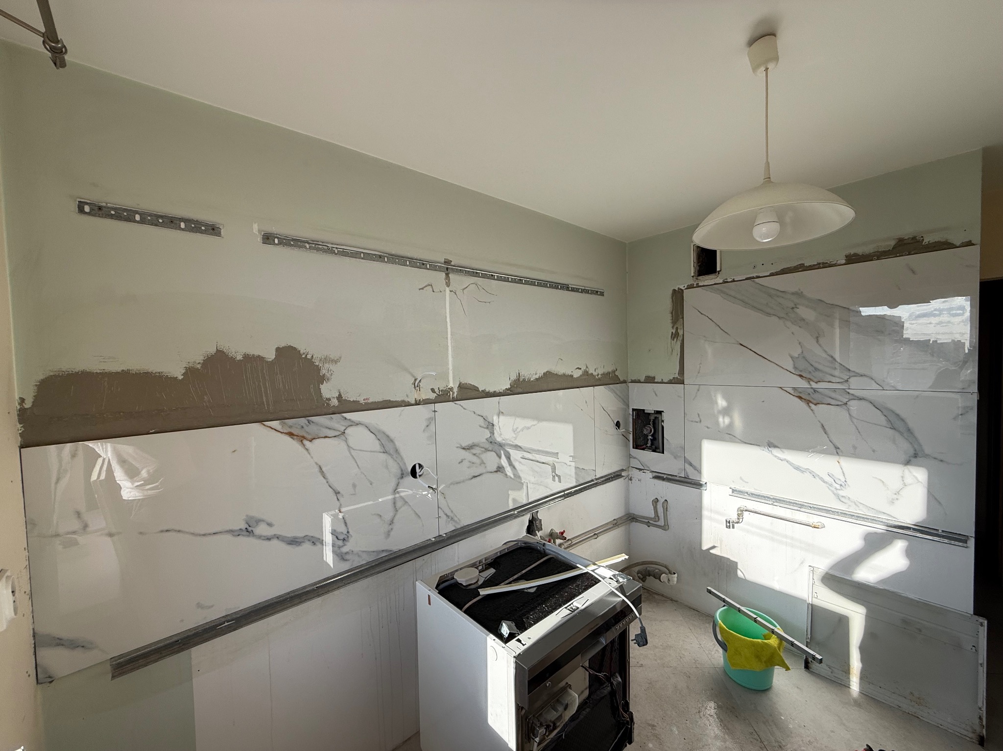 Układanie płytek imitujących marmur w kuchni w Piekary Śląskie. Widoczne metalowe listwy i niedokończone fugi. Prace wykończeniowe w toku.