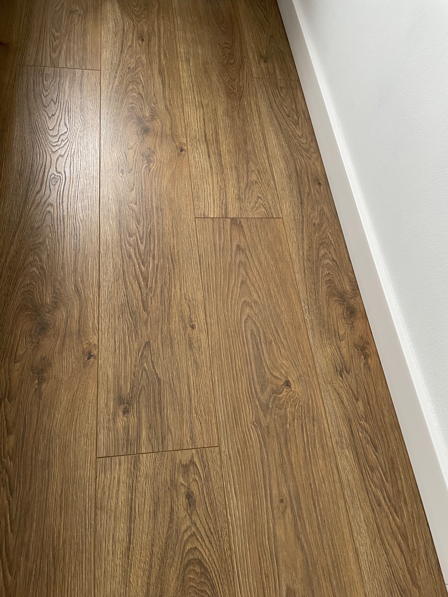 Ułożone panele podłogowe o wzorze drewna, widoczne łączenia, listwa przypodłogowa w kolorze białym.