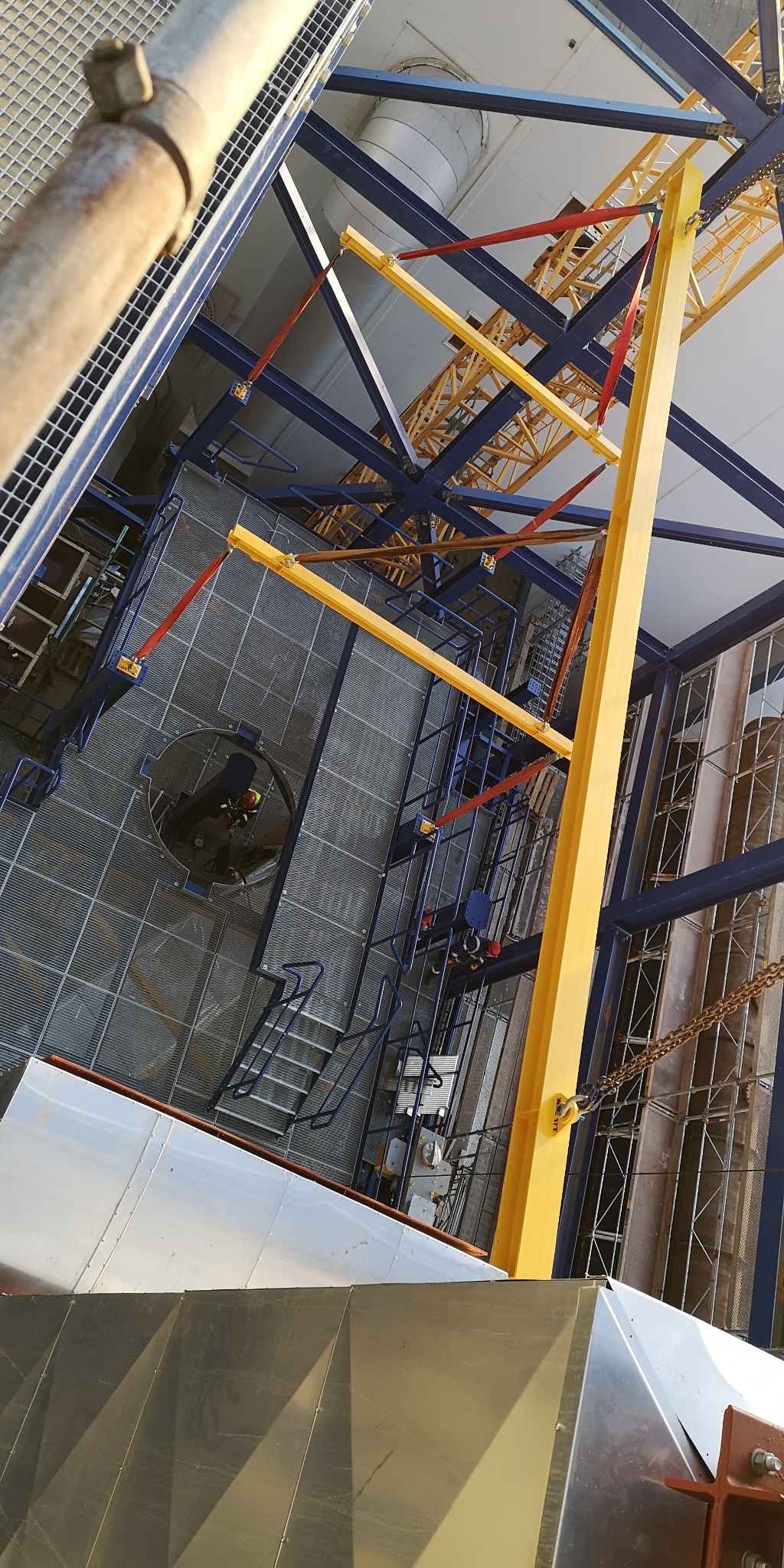 Montaż konstrukcji stalowej w Pysznicy z użyciem dźwigu. Widok z góry na elementy niebieskie i żółte oraz siatkową podłogę.