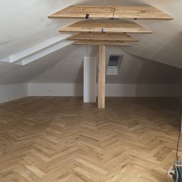Perfect Wall - Poddasze z drewnianą podłogą ułożoną w jodełkę, drewnianymi belkami pod sufitem i ścianami pomalowanymi na biało, widoczne przewody elektryczne.