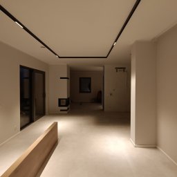 Perfect Wall - Wnętrze przestronnego, jasnego pomieszczenia z minimalistycznym wykończeniem, oświetleniem szynowym na suficie i kominkiem w oddali.