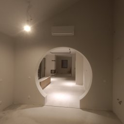 Perfect Wall - Wnętrze domu we Wrocławiu po pracach wykończeniowych, z okrągłym przejściem w ścianie, świeżo pomalowane na jasny kolor, widoczny klimatyzator i surowa podłoga.