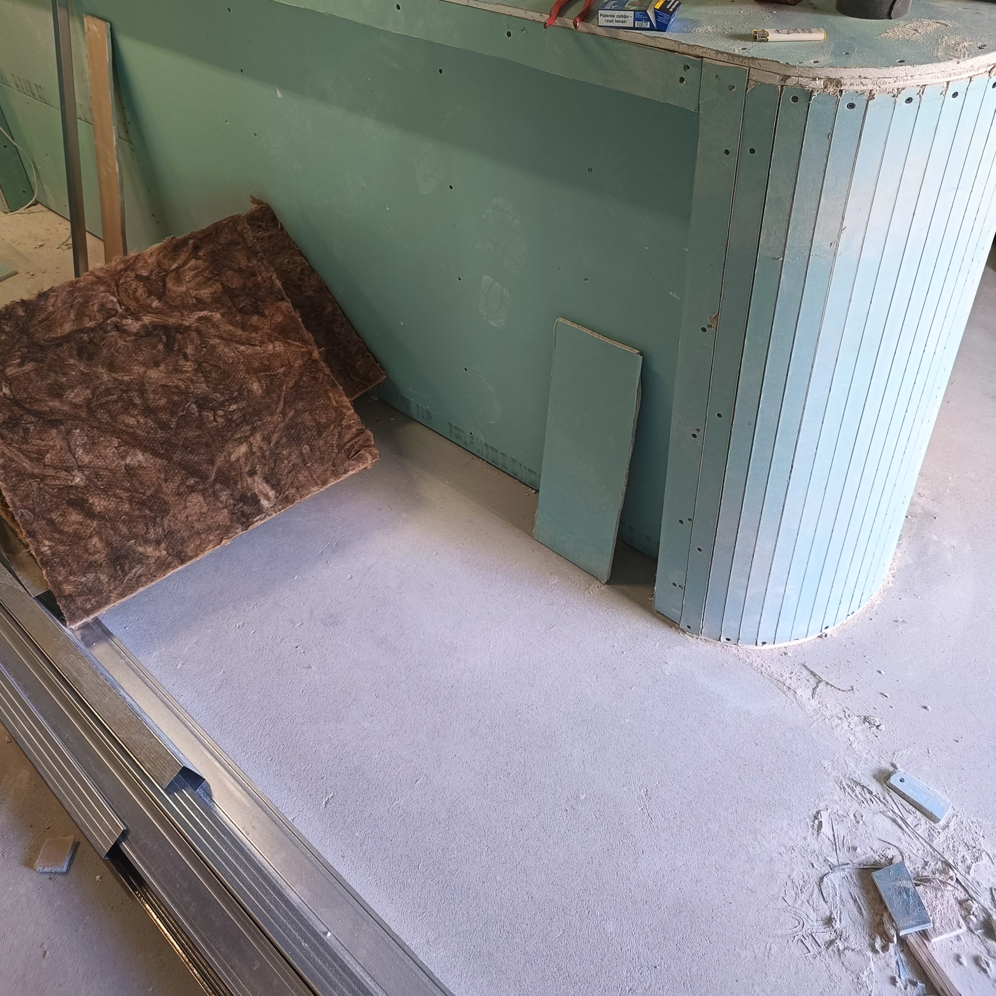 Wnętrze w trakcie prac wykończeniowych: płyty gipsowo-kartonowe tworzą zaokrągloną konstrukcję, obok leżą materiały izolacyjne i profile metalowe.