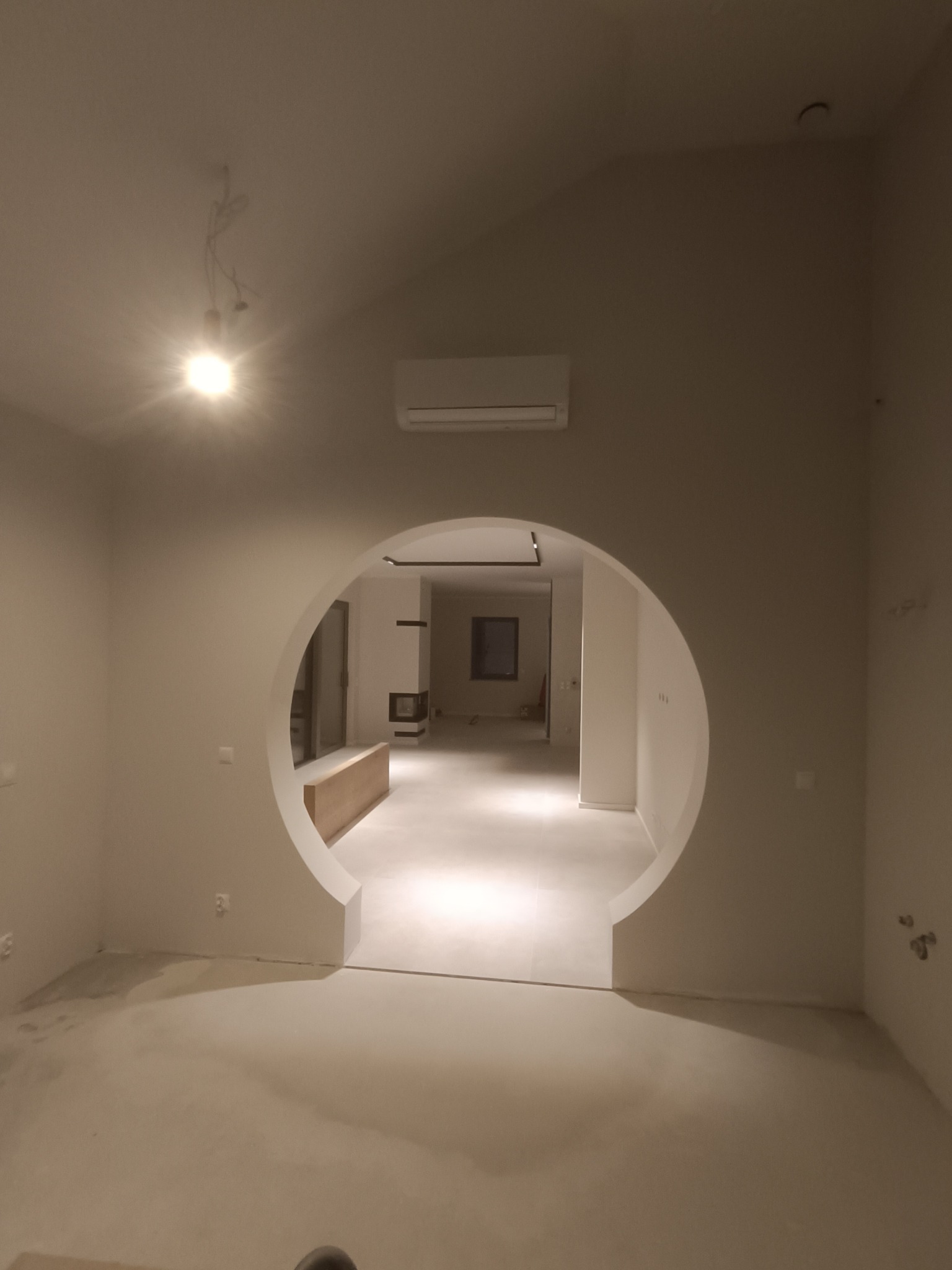 Wnętrze domu we Wrocławiu po pracach wykończeniowych, z okrągłym przejściem w ścianie, świeżo pomalowane na jasny kolor, widoczny klimatyzator i surowa podłoga.