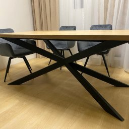 METAL FUSION - Stół z jasnym blatem i czarną, metalową podstawą w kształcie litery X, otoczony trzema szarymi krzesłami na tle okna z białymi zasłonami.