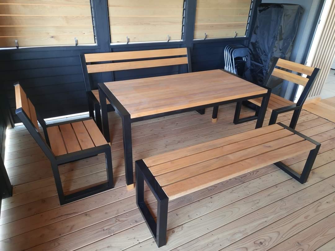 Zestaw mebli ogrodowych: stół z blatem z jasnego drewna i czarną metalową ramą, dwie krzesła z drewnianymi siedziskami i oparciami oraz czarnymi metalowymi ramami, ławka z drewnianym siedziskiem...