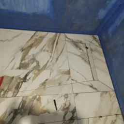 Montaż płytek imitujących marmur w kabinie prysznicowej z odpływem liniowym, widoczna hydroizolacja ścian, poziomica na płytkach.