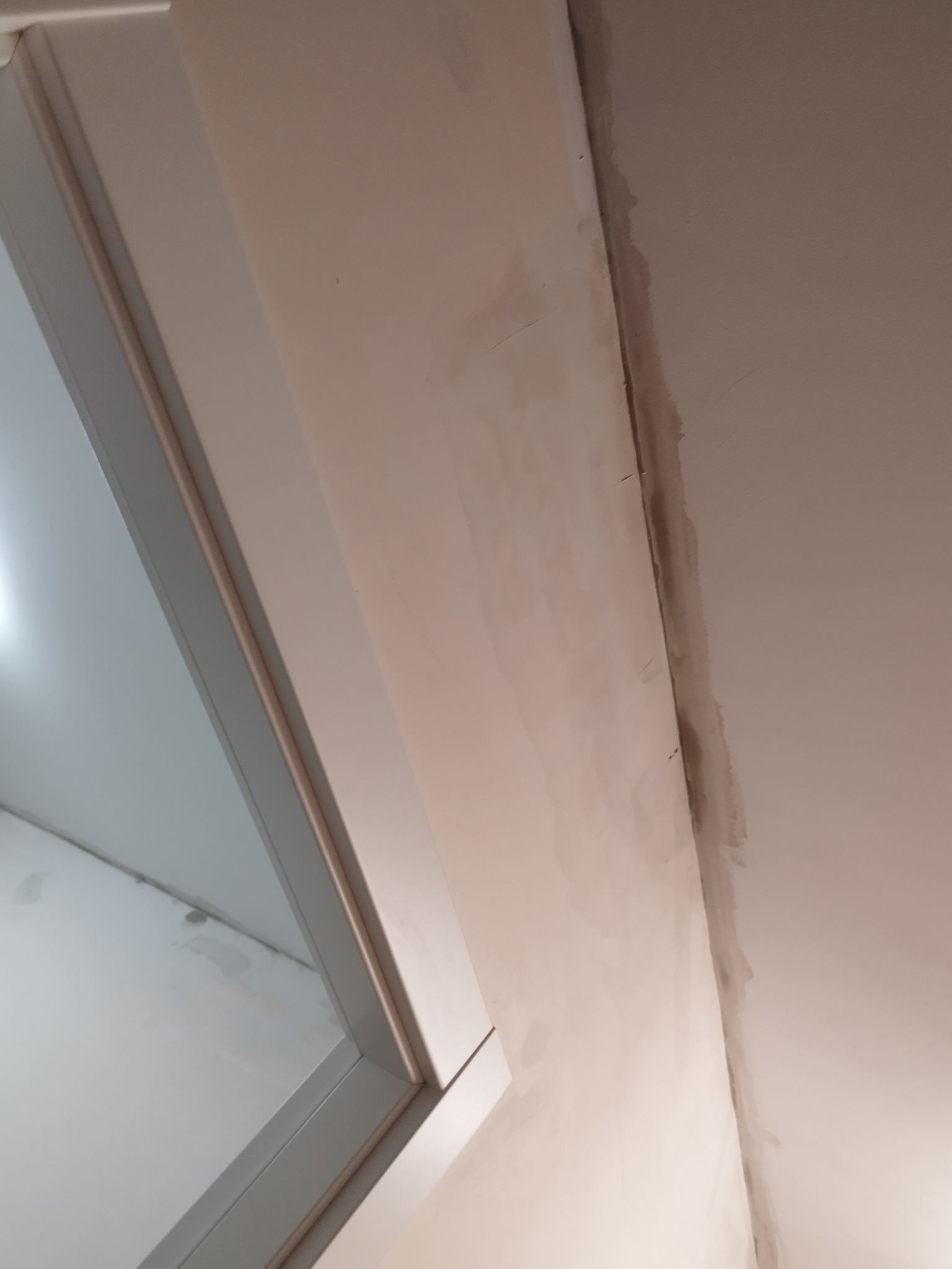 Ściana po szpachlowaniu, widoczne niedoskonałości i przejścia między warstwami, przygotowana do dalszej obróbki, narożnik okna po lewej stronie.