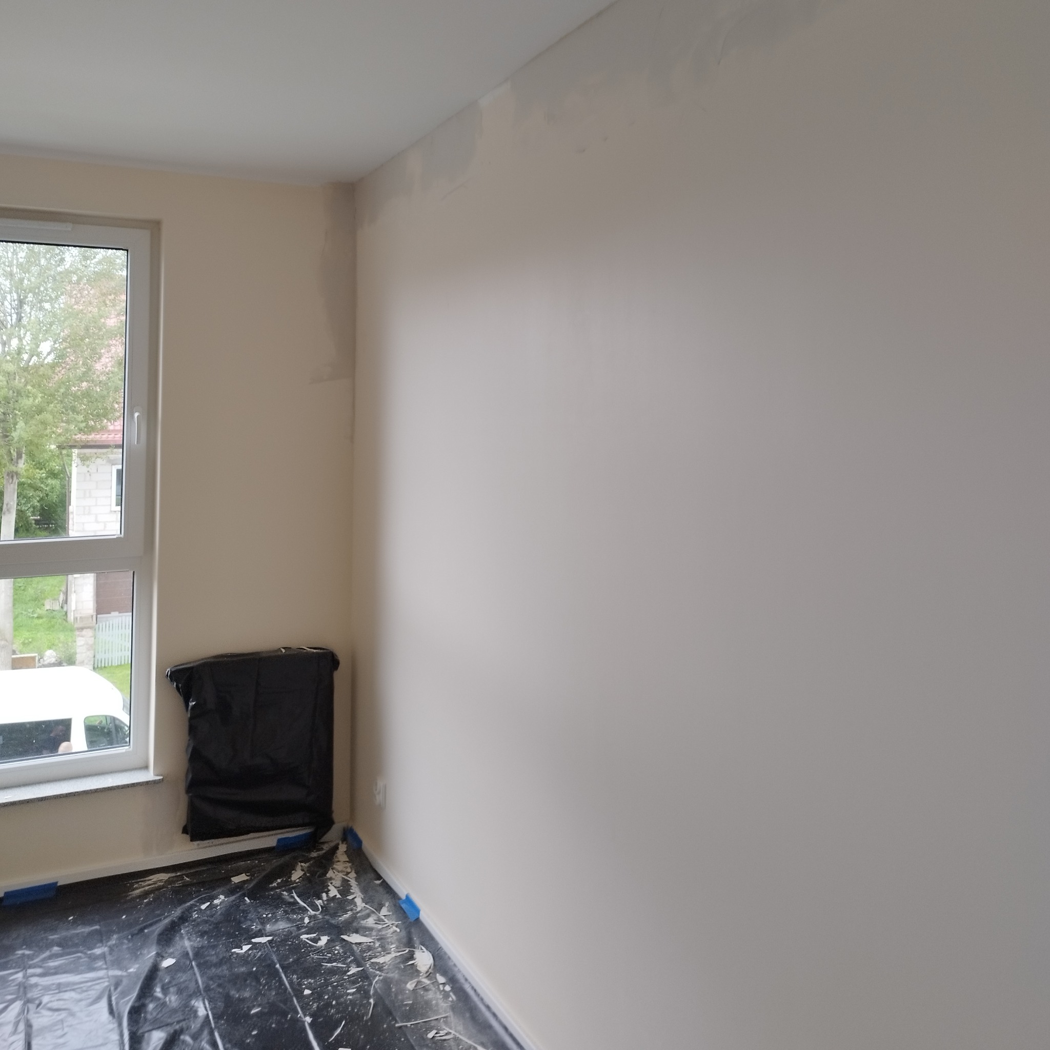 Pokój w trakcie szpachlowania ścian na gładko, zabezpieczona podłoga folią malarską, okno po lewej stronie.