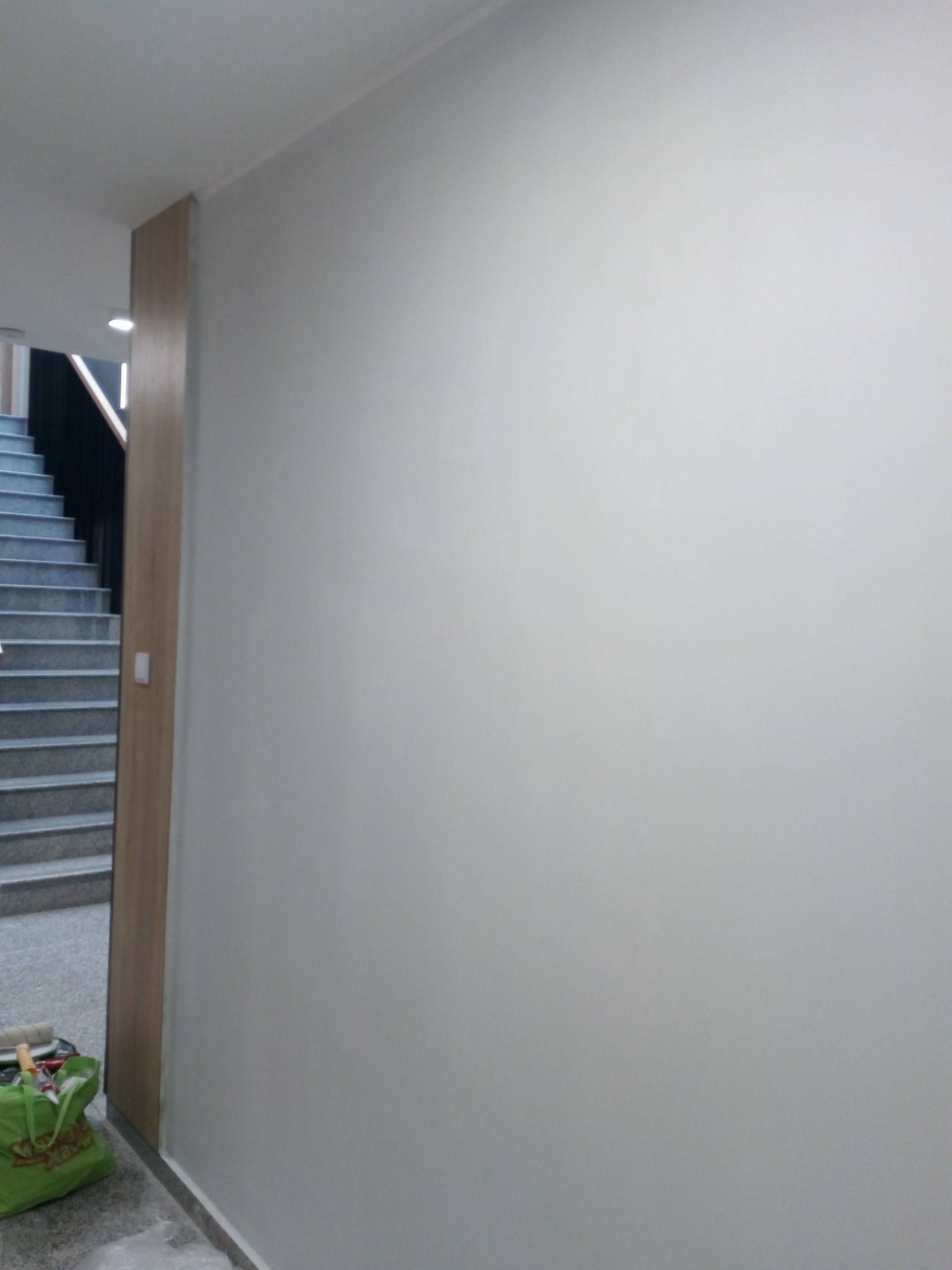 Świeżo pomalowana, gładka, biała ściana w korytarzu, widoczne schody i torba z narzędziami malarskimi u dołu.