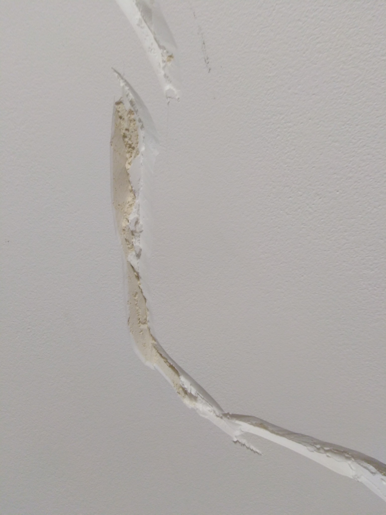 Uszkodzona, łuszcząca się warstwa wykończeniowa sufitu, ukazująca warstwy podkładowe i nierówności.