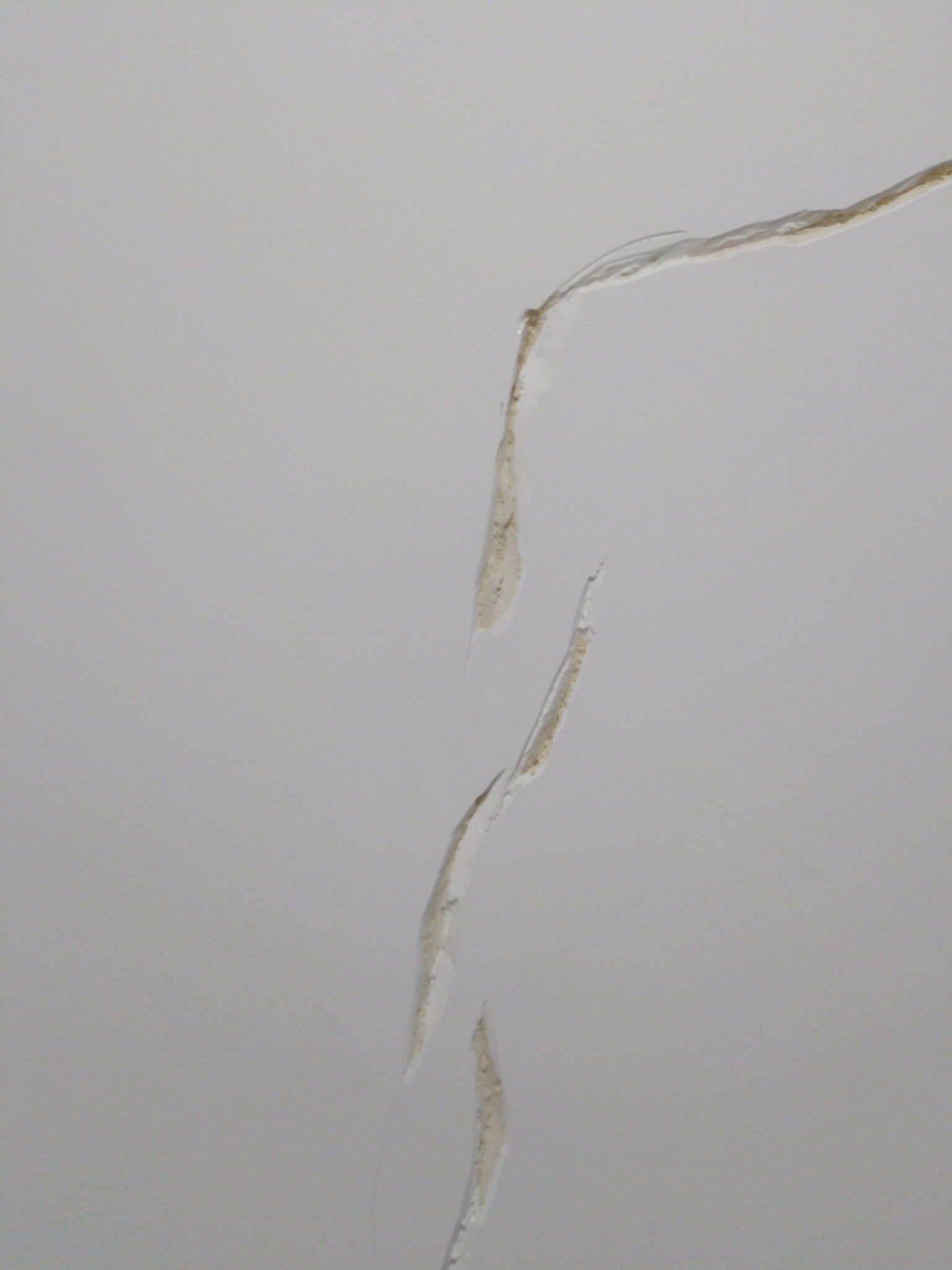 Uszkodzona, pęknięta i odspojona warstwa gładzi na suficie, widoczne warstwy podkładowe.