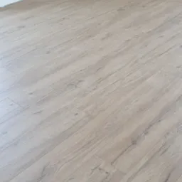 Jasne panele podłogowe ułożone w pokoju, w tle kartony paneli Swiss Krono Floors, taśma klejąca i narzędzia, niebieska pianka podkładowa w rogu.