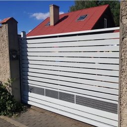 Loftski Poznań bramy przęsła balustrady - Nowoczesna, przesuwna brama wjazdowa z poziomych, białych profili, z ażurowym panelem wentylacyjnym u dołu, zamontowana między betonowymi słupkami z czarną skrzynką na listy