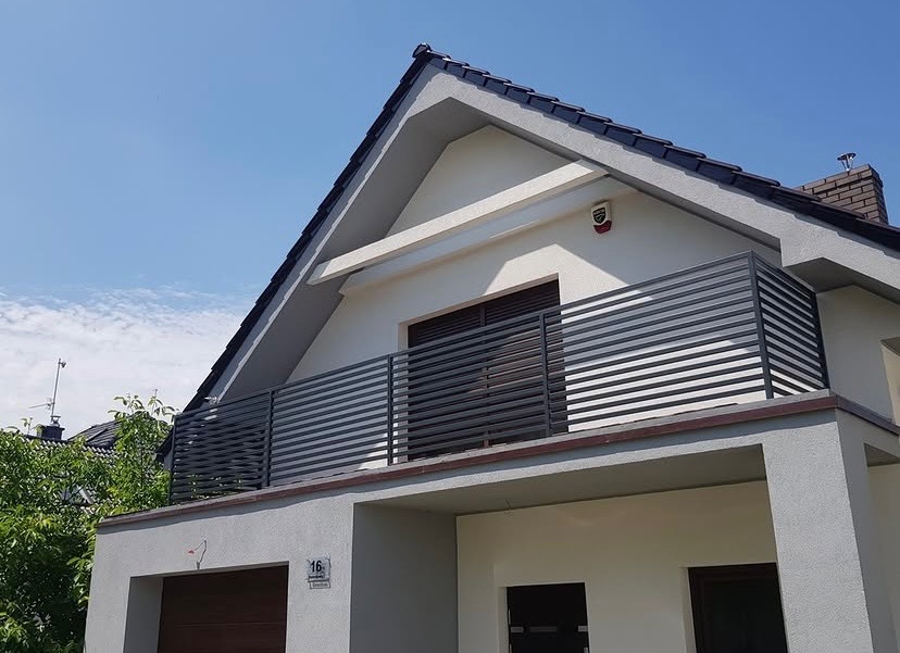 Nowoczesna balustrada balkonowa z poziomych profili, szara kolorystyka, widok na dwupiętrowy dom z garażem w słoneczny dzień.