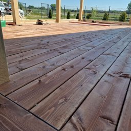 WoodBuild - Brązowe deski tarasowe ułożone pod lekkim kątem, z widocznymi słupami konstrukcji i narzędziami w tle, sugerujące świeżo zakończone prace.