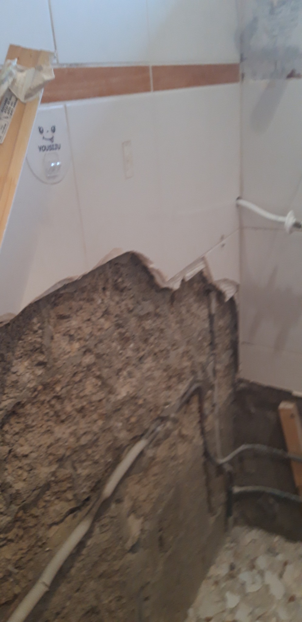 Niedokończona ściana łazienki z widoczną instalacją elektryczną i fragmentem starej glazury, przygotowywana do dalszych prac wykończeniowych.